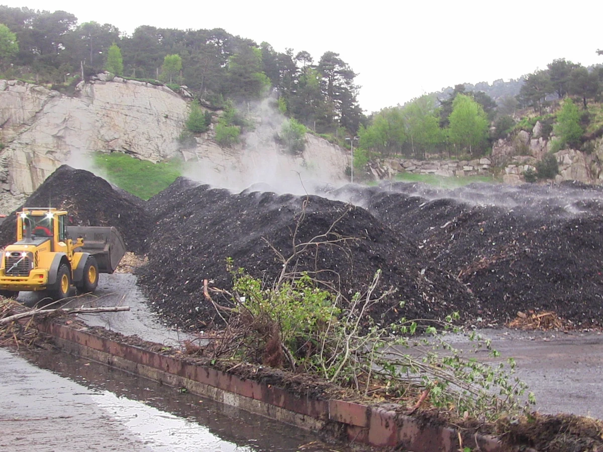 Plant residues, organic-material windrows and a loader at a commercial composting site — representative feedstock-handling environment